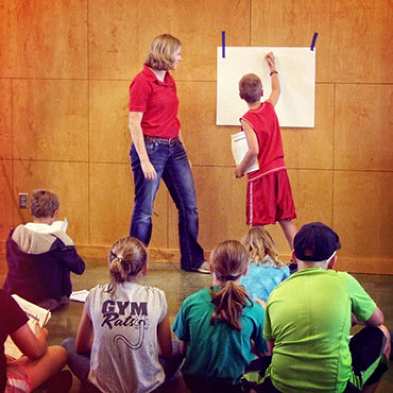 student writing on paper in front of classroom